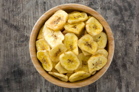Banana chips in bowl on wooden table. Top viewの写真素材