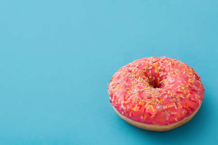 Pink frosted donut with colorful sprinkles on blue background. Copyspaceの写真素材