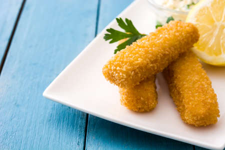crispy fried fish fingers with lemon and willow on blue wooden backgroundの写真素材