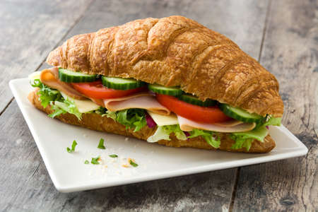 Croissant sandwich with cheese, ham and vegetables on wooden tableの写真素材