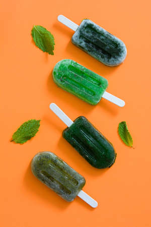 Green frozen ice pop on orange background. Top view