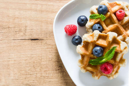 Traditional belgian waffles with blueberries and raspberries on wooden table. Top view Copyspaceの写真素材