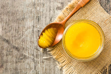 Ghee or clarified butter in jar and wooden spoon on wooden table. Top view Copyspace