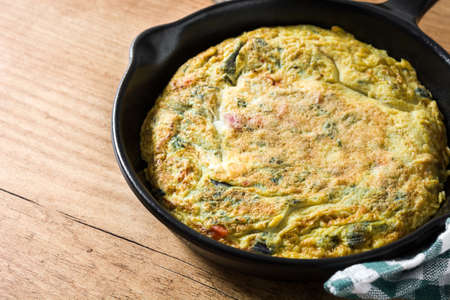 Frittata made of eggs and vegetables in a pan, on wooden table.
