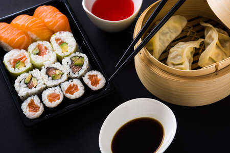 Dumplings or gyoza served in traditional steamer and sushi on black background. Close upの写真素材