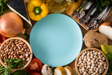 Healthy eating. Mediterranean diet. Fruit, vegetables, grain, nuts olive oil and fish on wooden table. Top view with copy space on plateの写真素材