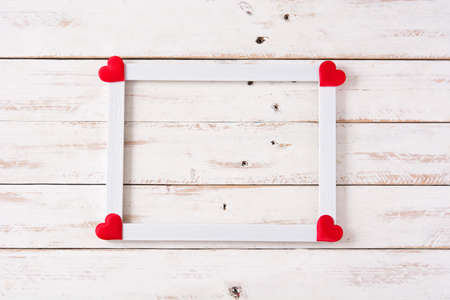 Mockup valentine's day concept.White frame decorated with hearts on white wooden table. Copyspace