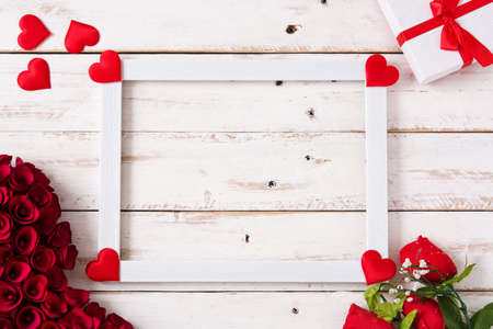 Mockup valentine's day concept.White frame decorated with hearts, roses and gift on white wooden table. Copyspaceの写真素材