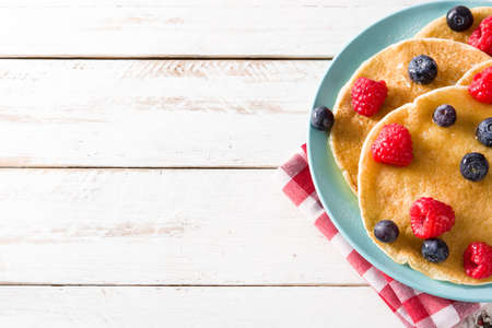 Pancakes with raspberries, blueberries and honey on white wooden table. Copyspace