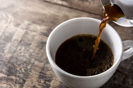 Pouring hot coffee in a cup on wooden table.の写真素材