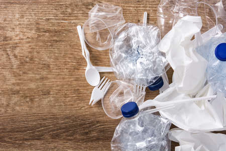 Disposable waste plastic on wooden background. Top view. Copyspace