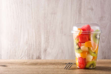 Fresh cut fruit in a plastic cup on wooden table. Copyspaceの写真素材