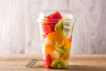 Fresh cut fruit in a plastic cup on wooden tableの写真素材