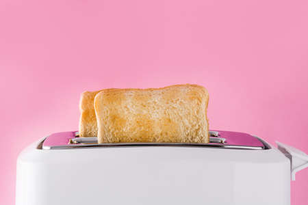Toasted toast bread in white toaster on pink background