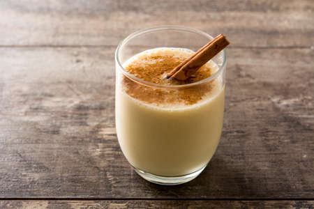 Homemade eggnog with cinnamon in glass on wooden table. Typical Christmas dessert.