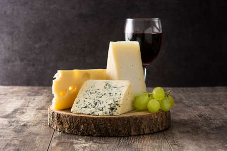 Assortment of cheeses and wine on wooden table.