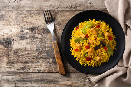 Fried rice with chicken and vegetables on black plate on wooden tableの写真素材