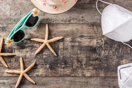 Sunglasses, starfish, summer hat and protective face mask on wooden background. Coronavirus summer concept.の写真素材