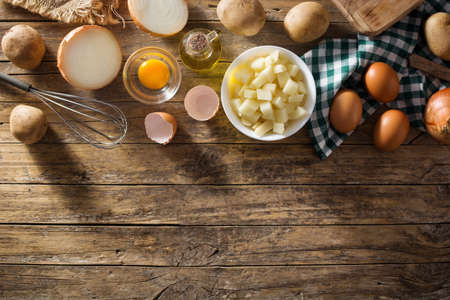 Spanish omelette tortilla ingredients: eggs, potatoes and onion on wooden background. Top view copy...