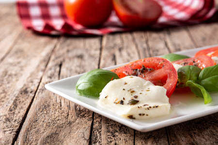Traditional caprese salad with tomato and mozzarella cheese on rustic wooden table