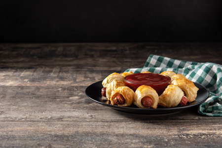 Pigs in blankets. Mini sausages wrapped in puff pastry with ketchup sauce on wooden tableの写真素材