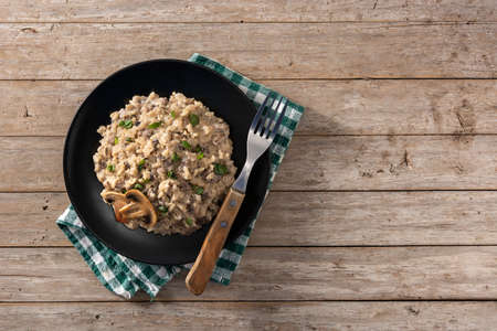 Risotto with mushroom on black plate on wooden table. Top view. Copy space