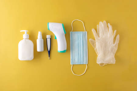 Medical gloves, disinfectant, thermometer, hand sanitizer and surgical mask on yellow backgroundの写真素材