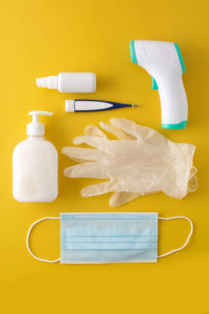 Medical gloves, disinfectant, thermometer, hand sanitizer and surgical mask on yellow backgroundの写真素材