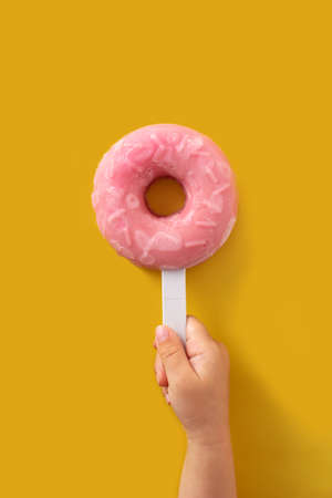 Hand holding a strawberry donut ice creams on yellow backgroundの写真素材