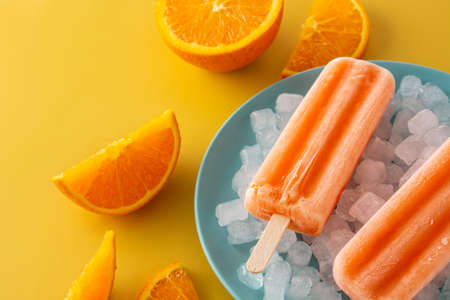 Orange popsicles on blue plate on yellow backgroundの写真素材