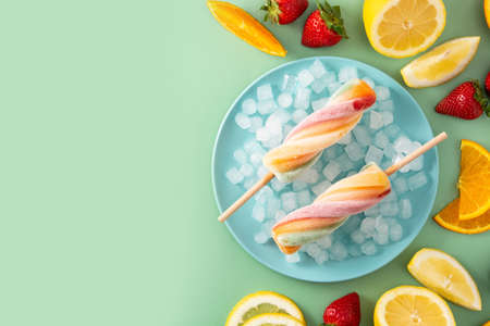 Spiral colorful ice lolly with fruit on green background
