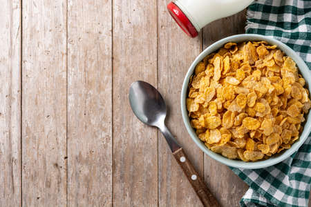 Corn flakes in a blue bowl and milk bottle on wooden table