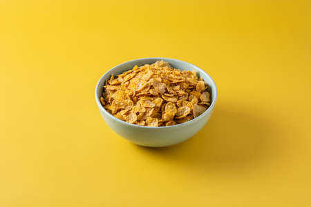 Corn flakes in a blue bowl on yellow background
