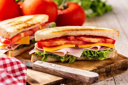 Sandwich with tomato, lettuce, ham and cheese on wooden tableの写真素材