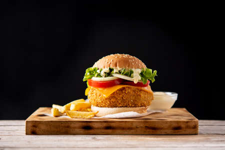 Crispy chicken burger with cheese and french fries on wooden tableの写真素材