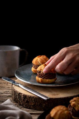 woman catching chocolate profiteroles on rustic wooden table