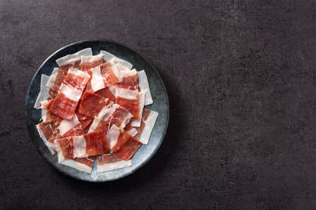 Spanish serrano ham slices on black plate on black slate backgroundの写真素材