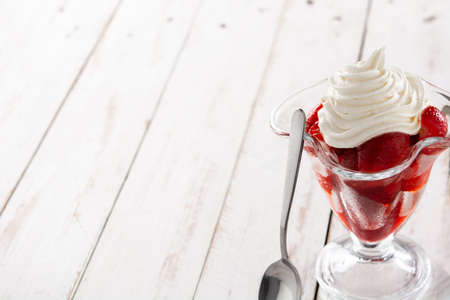 Strawberries and whipped cream in ice cream glass on wooden tableの写真素材