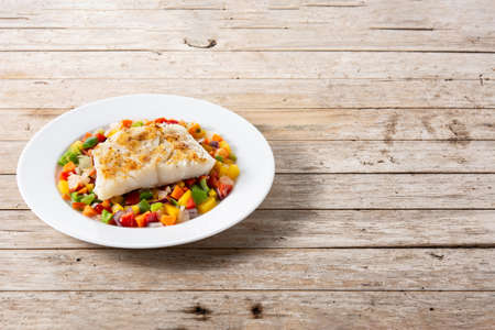 Grilled cod with vegetables in plate on wooden table