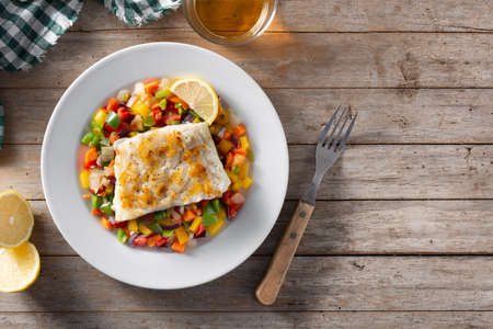 Grilled cod with vegetables in plate on wooden table