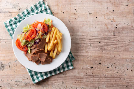 Plate of kebab, vegetables and french fries on wooden tableの写真素材
