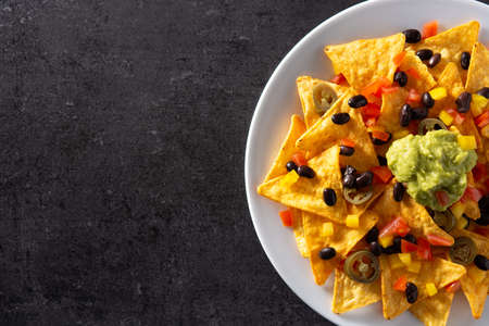 Mexican nachos tortilla chips with black beans, guacamole, tomato and jalapeno on black backgroundの写真素材