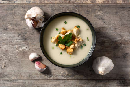 Garlic soup topped with croutons in black bowl on wooden tableの写真素材
