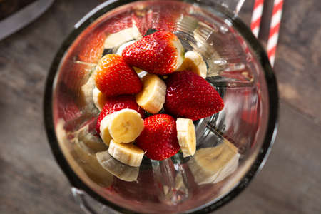 Preparing strawberry and banana smoothie in mixer on wooden tableの写真素材