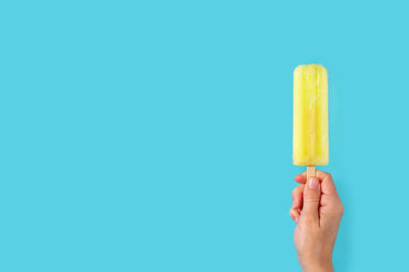 Hand holding a lemon  ice cream stick on blue background