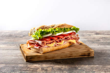 Submarine sandwich with ham, cheese, lettuce, tomatoes, onion, mortadella and sausage on wooden tableの写真素材