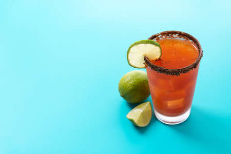 Homemade michelada cocktail with beer, lime juice, hot sauce, salted rim and tomato juice on blue backgroundの写真素材