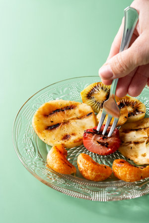 close-up of a hand picking roasted fruit with a fork on a green backgroundの写真素材