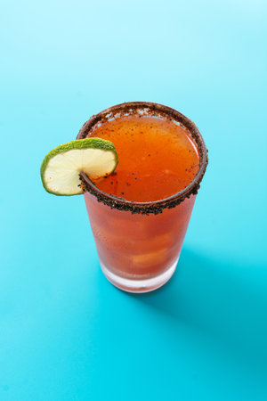 Homemade michelada cocktail with beer, lime juice, hot sauce, salted rim and tomato juice on blue backgroundの写真素材
