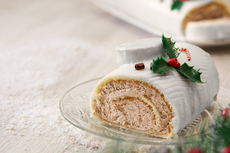 White chocolate yule log cake with christmas lights and ornaments on wooden tableの写真素材